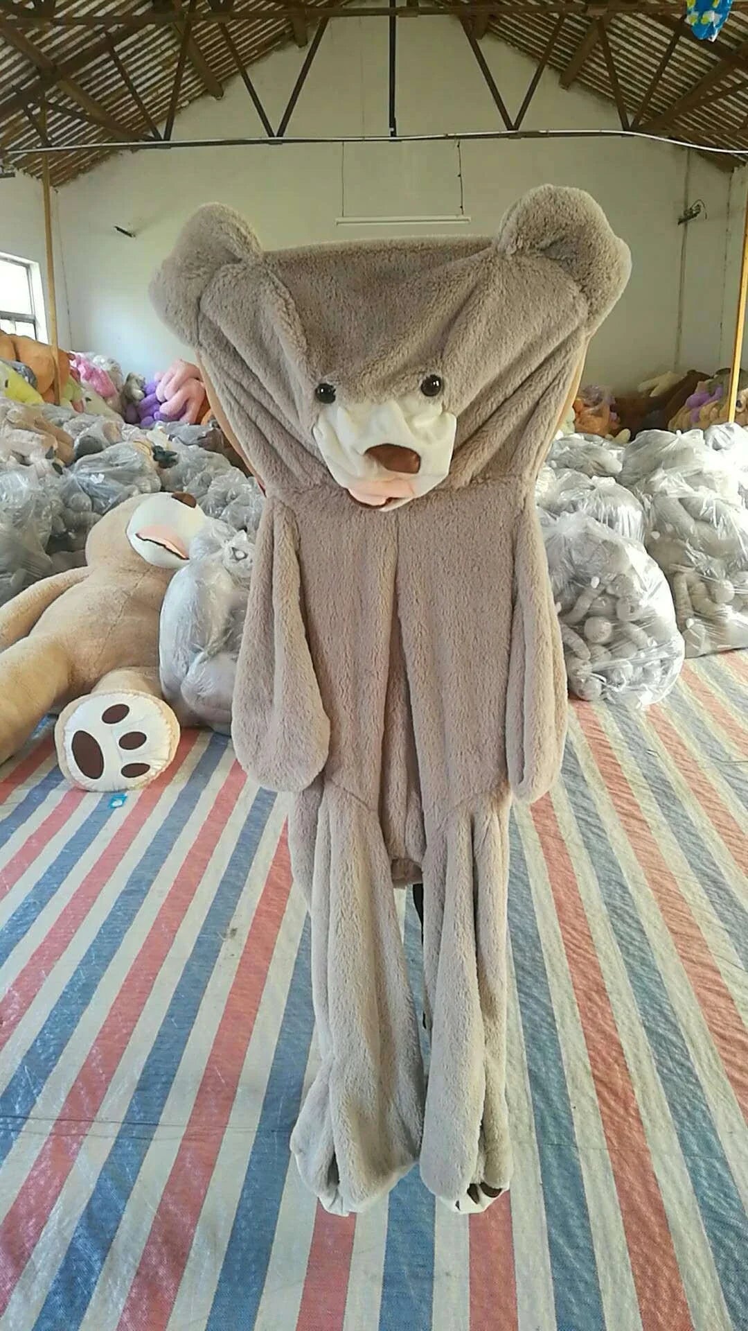 Colossal plush teddy bear in various sizes and colors, including light brown, dark brown, gray, white, pink, and purple