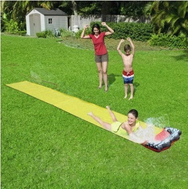 Kids playing on a yellow inflatable water slide in a backyard garden setting