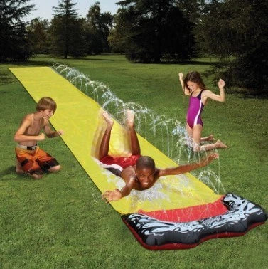 Kids playing on a yellow inflatable water slide in a backyard garden setting