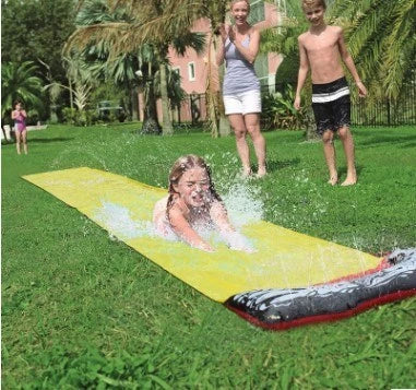 Kids playing on a yellow inflatable water slide in a backyard garden setting