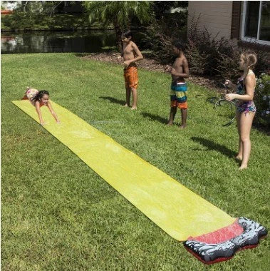 Kids playing on a yellow inflatable water slide in a backyard garden setting