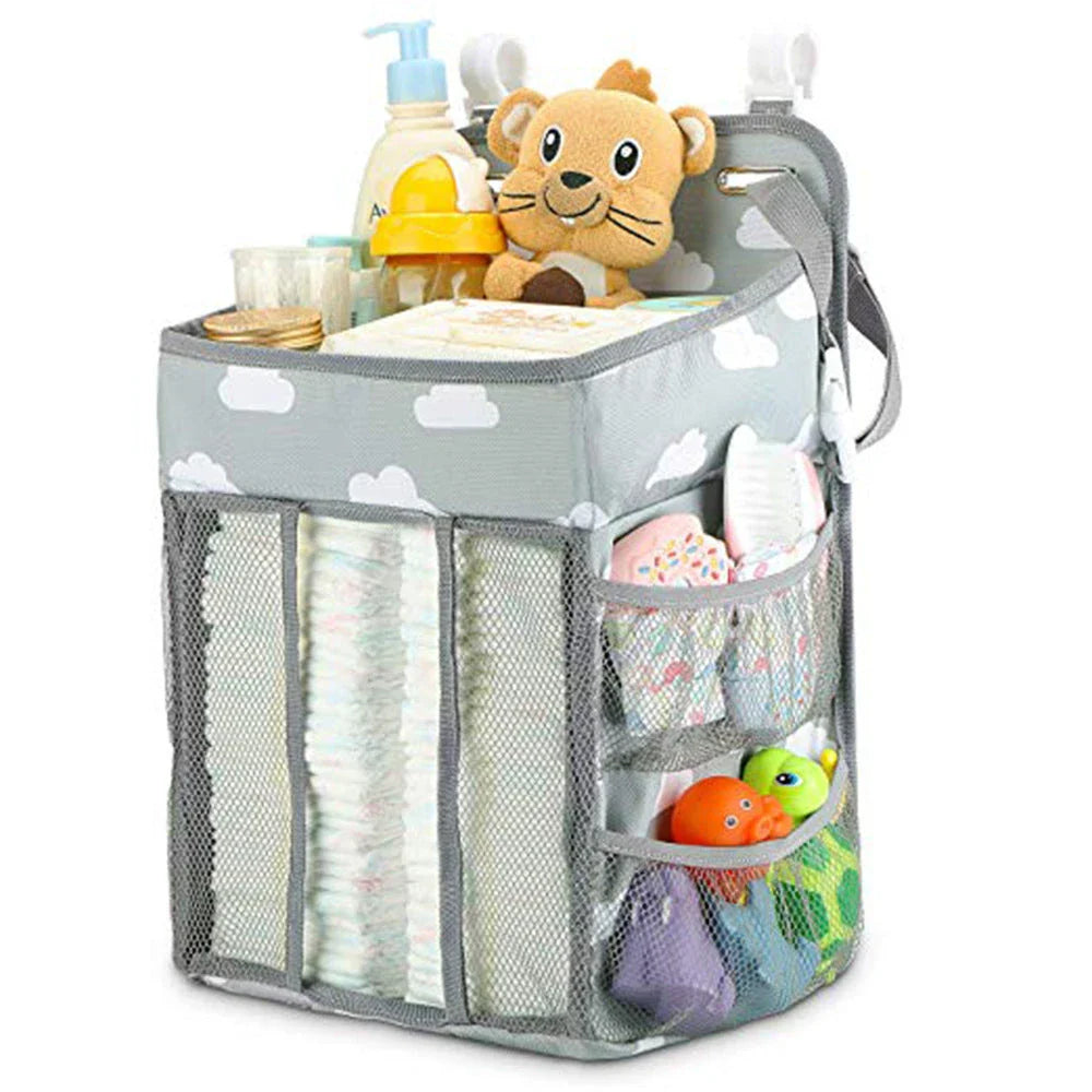 A gray crib-side organizer hanging on a white crib, storing various baby items like diapers, bottles, and toys.