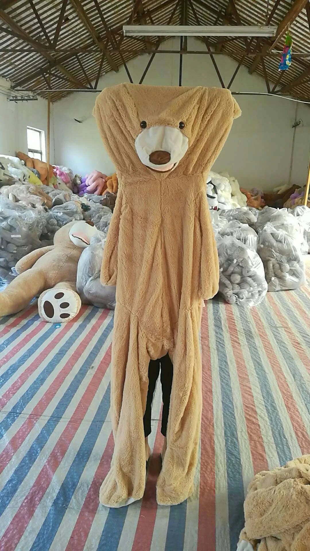 Colossal plush teddy bear in various sizes and colors, including light brown, dark brown, gray, white, pink, and purple