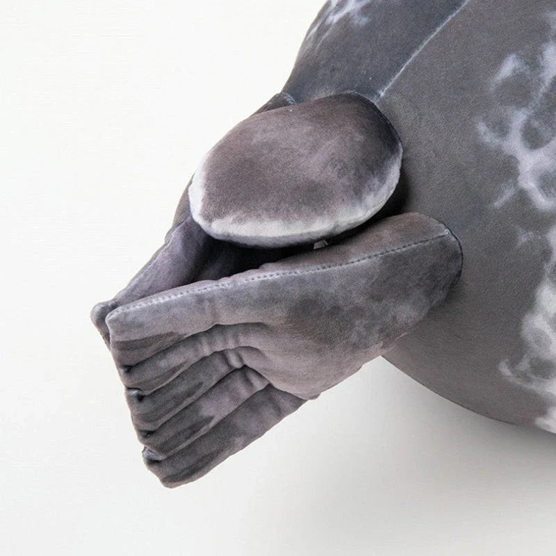 A plush, soft, and cuddly grey or white seal-shaped cushion with a detailed, lifelike design