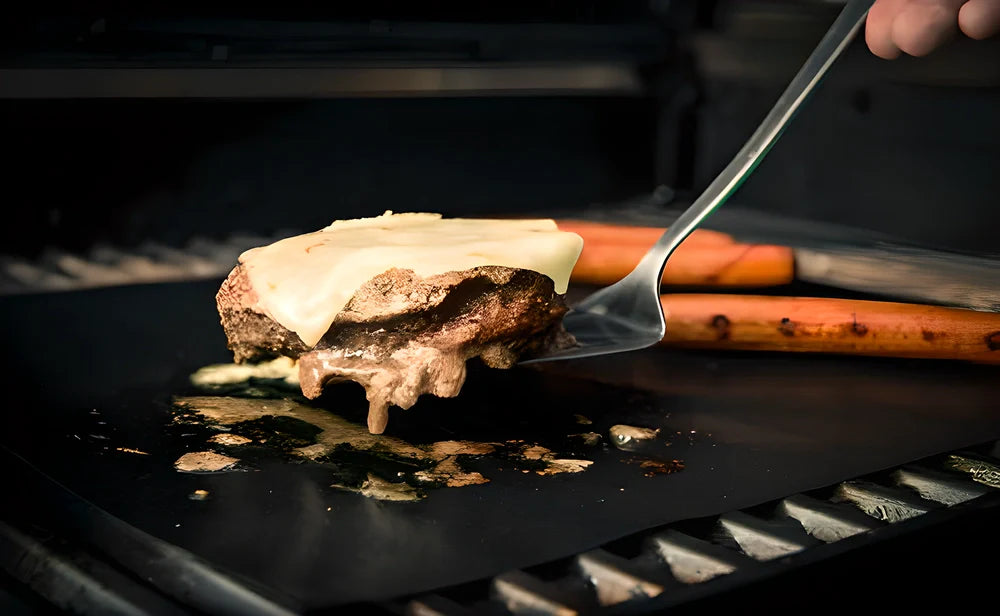 Two black nonstick BBQ grill mats on a grill, perfect for retaining juices and flavours while preventing food loss.