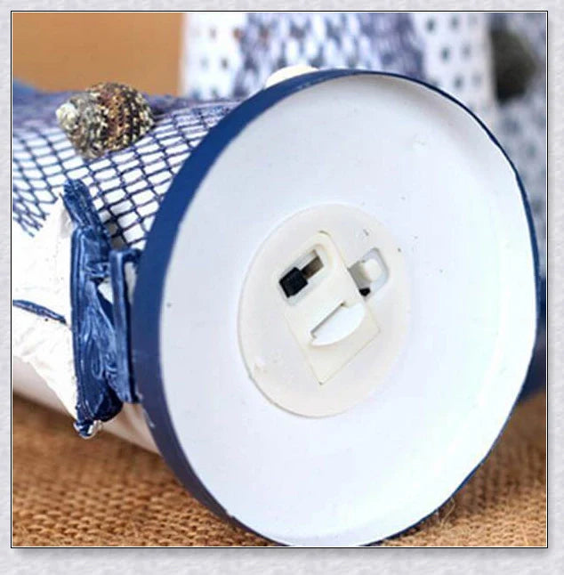 Oceanica LED Lighthouse Lantern Nightlight with nautical details like a small boat, life buoy, and seashells, providing a soft warm glow.