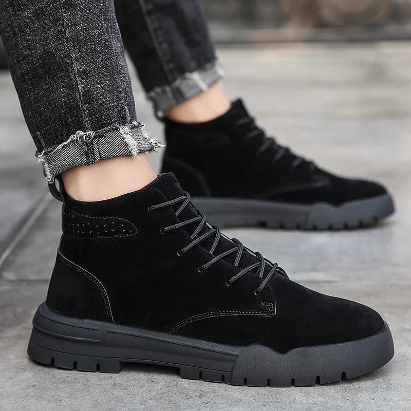A pair of black, suede British-style Martin boots with a thick, rubber sole and round toe shape.