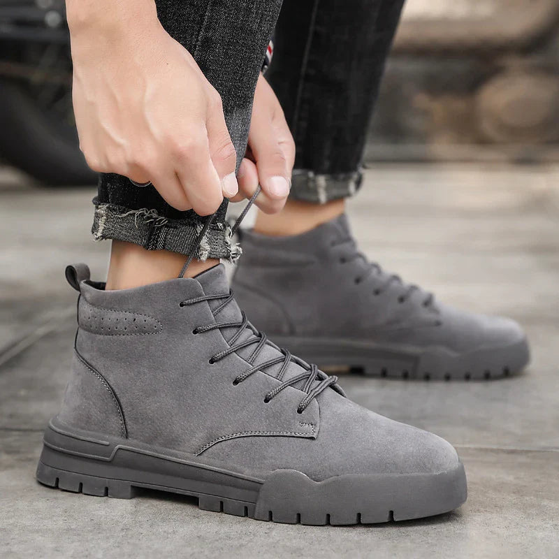 A pair of black, suede British-style Martin boots with a thick, rubber sole and round toe shape.