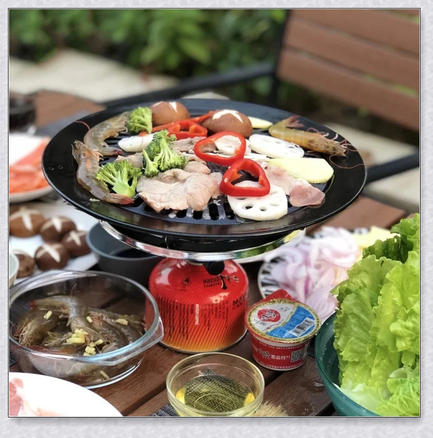 Hunters Creek Portable Korean Outdoor Barbecue Gas Grill Pan with various cooking accessories, including a baking tray, kettle, and pot