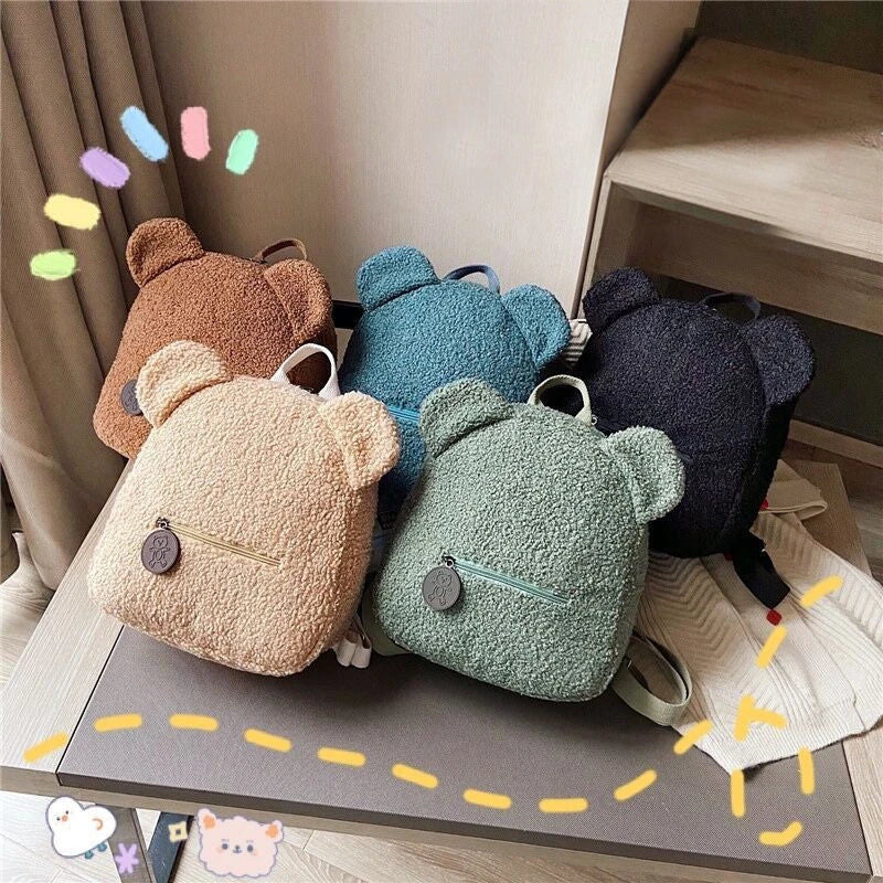 Adorable bear-shaped backpack made of soft fleece material in various colors, featuring a spacious main compartment and adjustable shoulder straps for comfortable wear.