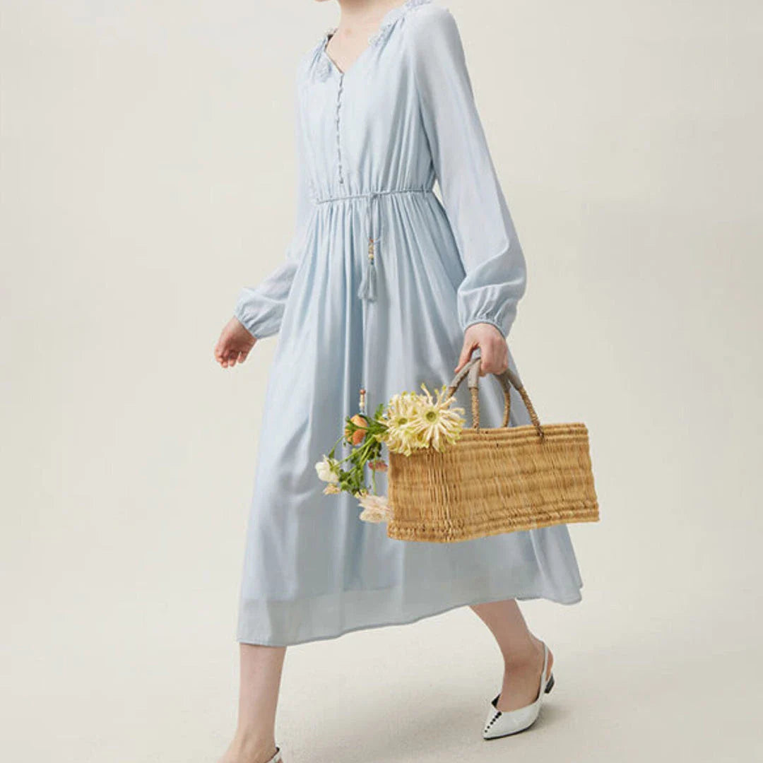 A woman wearing a long-sleeved, midi-length dress in a French pastoral style with an empire waistline and A-line silhouette.