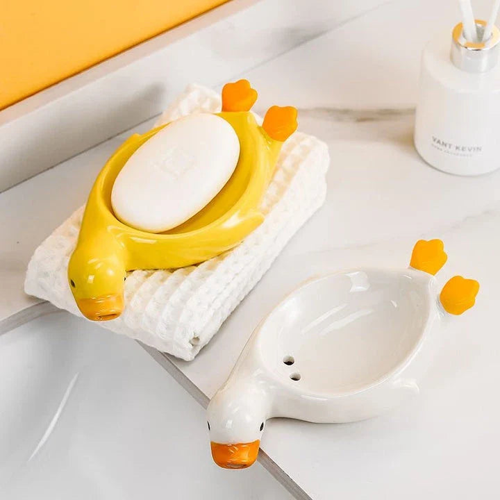 A yellow duck-shaped ceramic soap dish with a drainage system, suitable for modern and traditional British bathrooms.