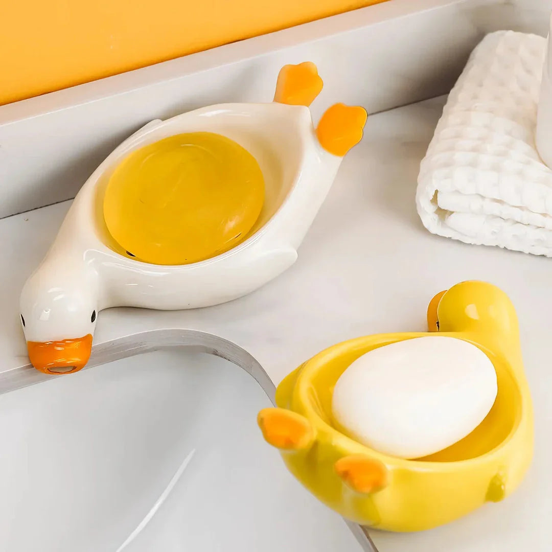 A yellow duck-shaped ceramic soap dish with a drainage system, suitable for modern and traditional British bathrooms.