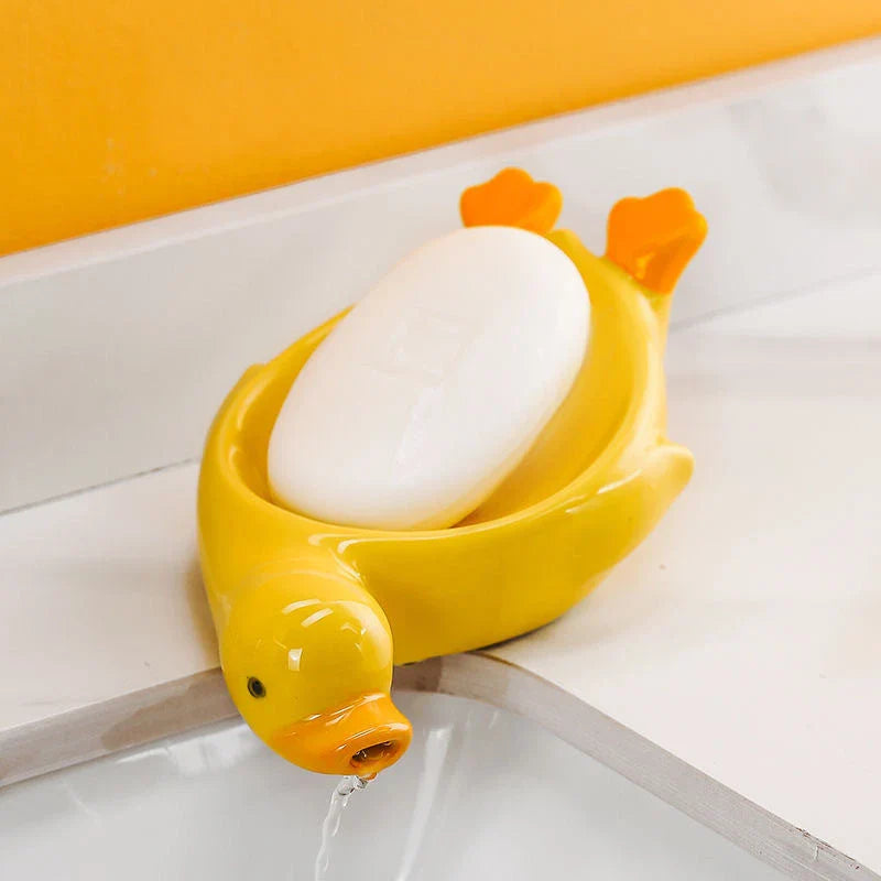A yellow duck-shaped ceramic soap dish with a drainage system, suitable for modern and traditional British bathrooms.