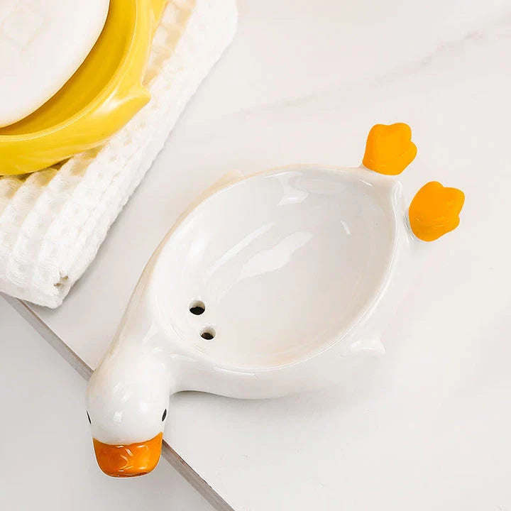 A yellow duck-shaped ceramic soap dish with a drainage system, suitable for modern and traditional British bathrooms.