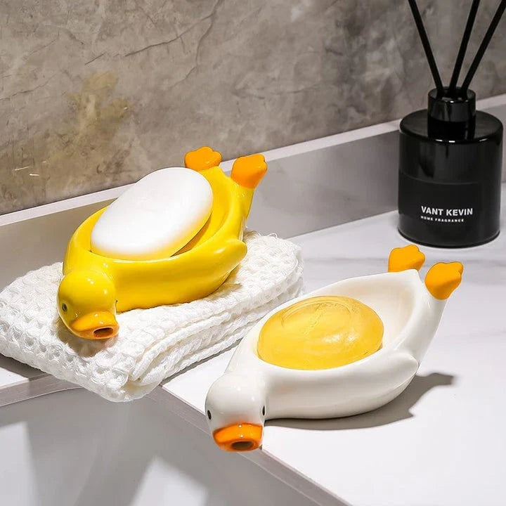 A yellow duck-shaped ceramic soap dish with a drainage system, suitable for modern and traditional British bathrooms.