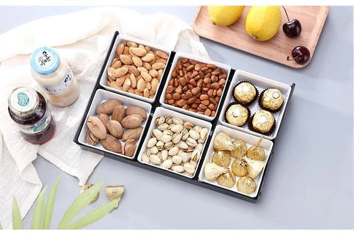 Premium British plastic snack trays in a variety of colours, including clear, white, and grey, with a black, white, or natural wood pallet for storage and display.
