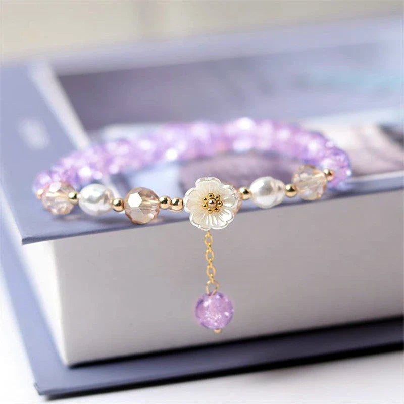 Elegant beaded bracelet with a white flower charm, vibrant purple crystal beads, and an adjustable design for a comfortable fit