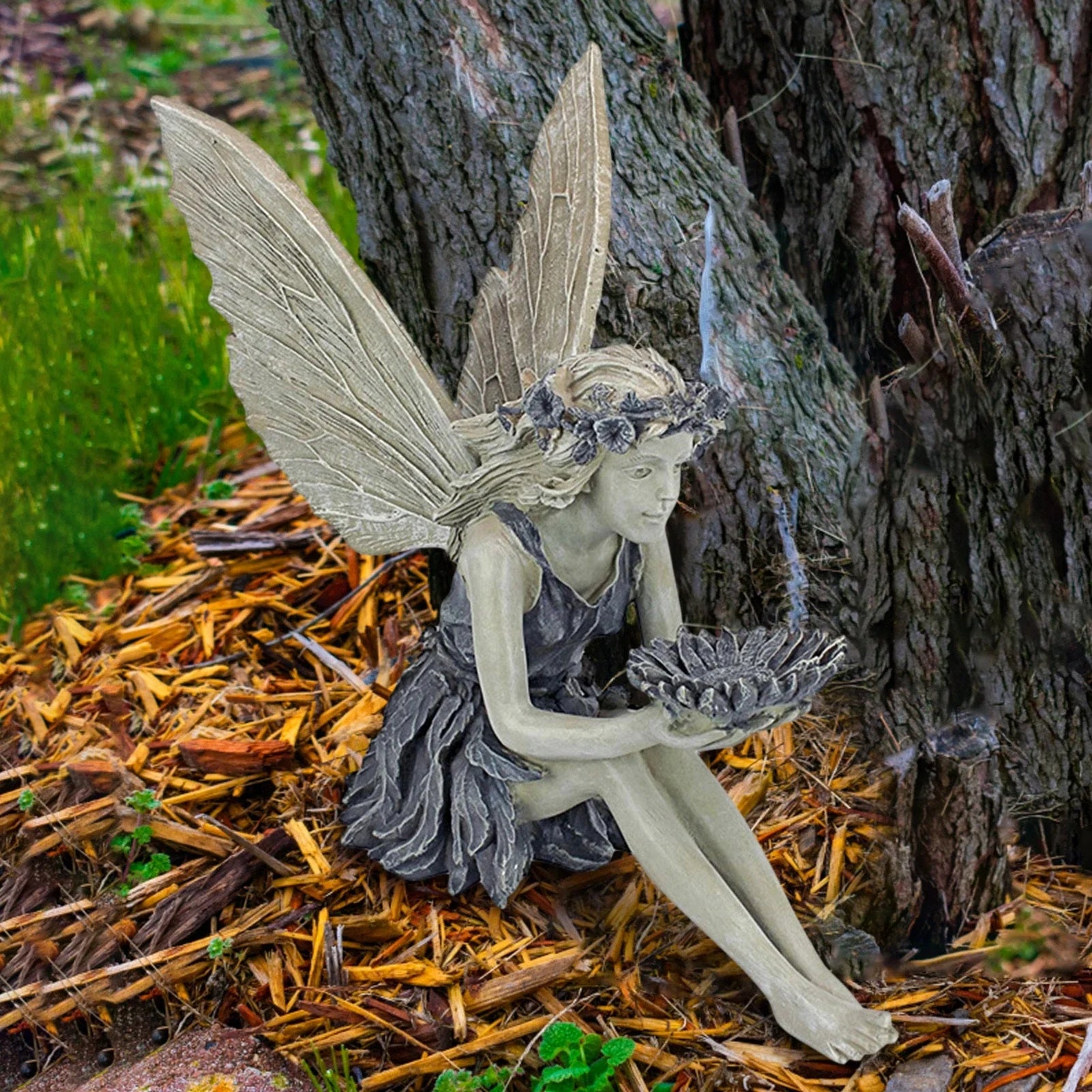 A beautiful resin fairy garden statue with a flower crown and petal skirt, holding a sunflower bowl to attract birds