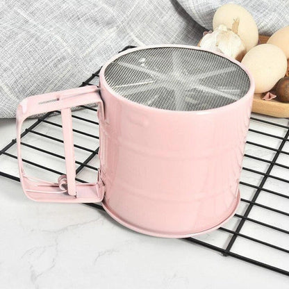 Stainless steel handheld baking flour sifter in a soft pink colour, designed for efficient sifting and aeration of dry ingredients for light and fluffy baked goods.