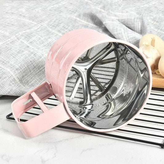 Stainless steel handheld baking flour sifter in a soft pink colour, designed for efficient sifting and aeration of dry ingredients for light and fluffy baked goods.