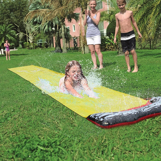 Kids playing on a yellow inflatable water slide in a backyard garden setting