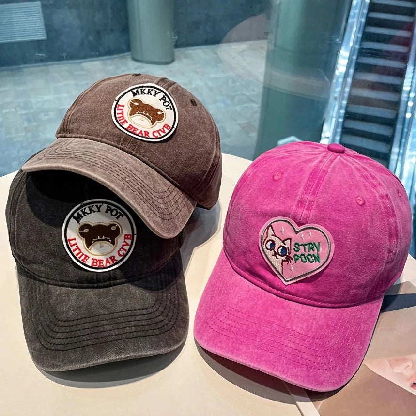 Two pink baseball caps with a cartoon love design, perfect for both women and men to add a touch of playful personality to their outfits.