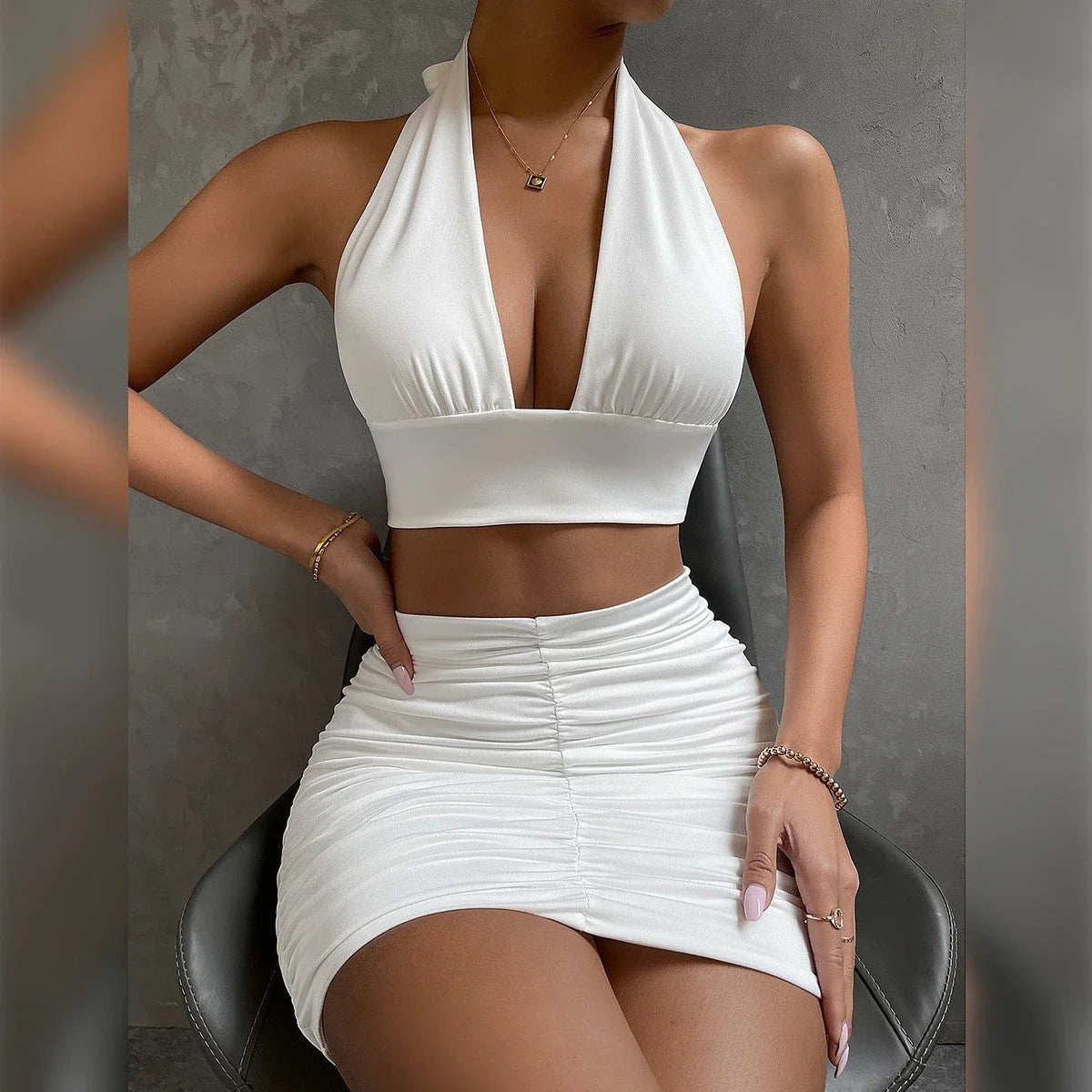 A stylish two-piece dress set featuring a halter-style lace-up top and a pleated hip-covering skirt, available in white, black, and pea green colors.