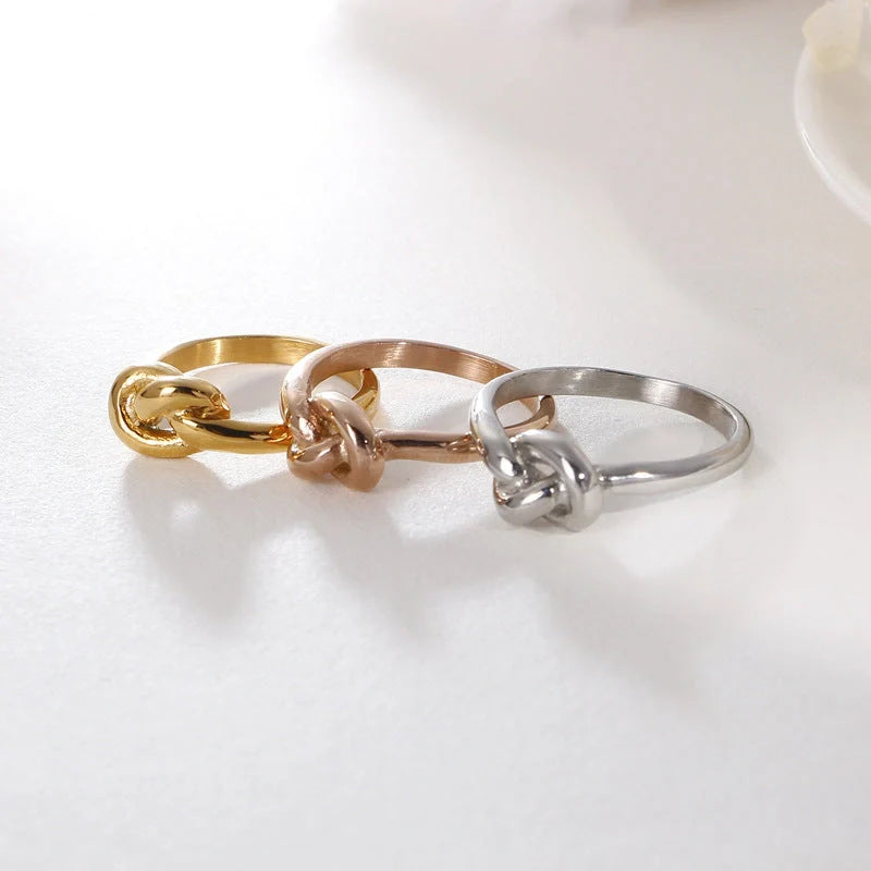 Sleek titanium steel geometric love knot ring in golden and rose gold colours, showcasing a modern and sophisticated design