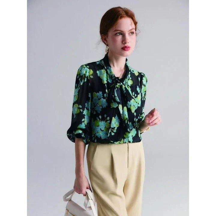 A close-up view of an elegant floral silk blend blouse with puff sleeves and a bow collar, showcasing its sophisticated British design.