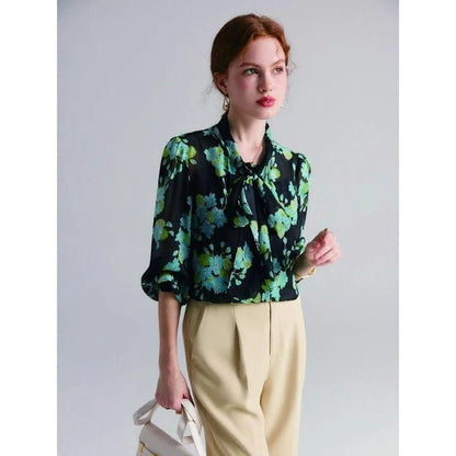 A close-up view of an elegant floral silk blend blouse with puff sleeves and a bow collar, showcasing its sophisticated British design.