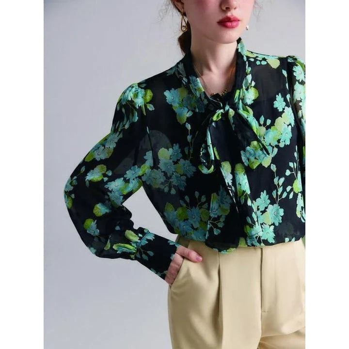 A close-up view of an elegant floral silk blend blouse with puff sleeves and a bow collar, showcasing its sophisticated British design.