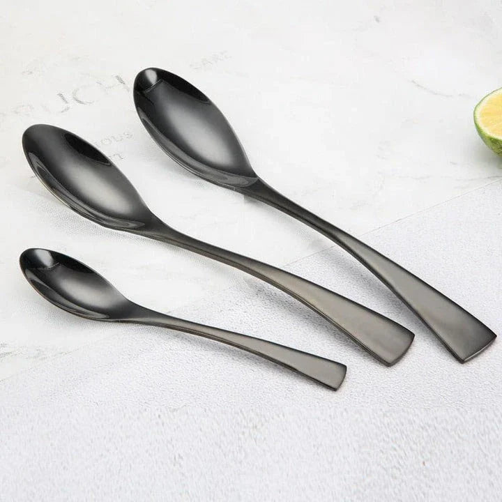 A stylish set of black stainless steel flatware, including a teaspoon, knife, and fork, on a white background.