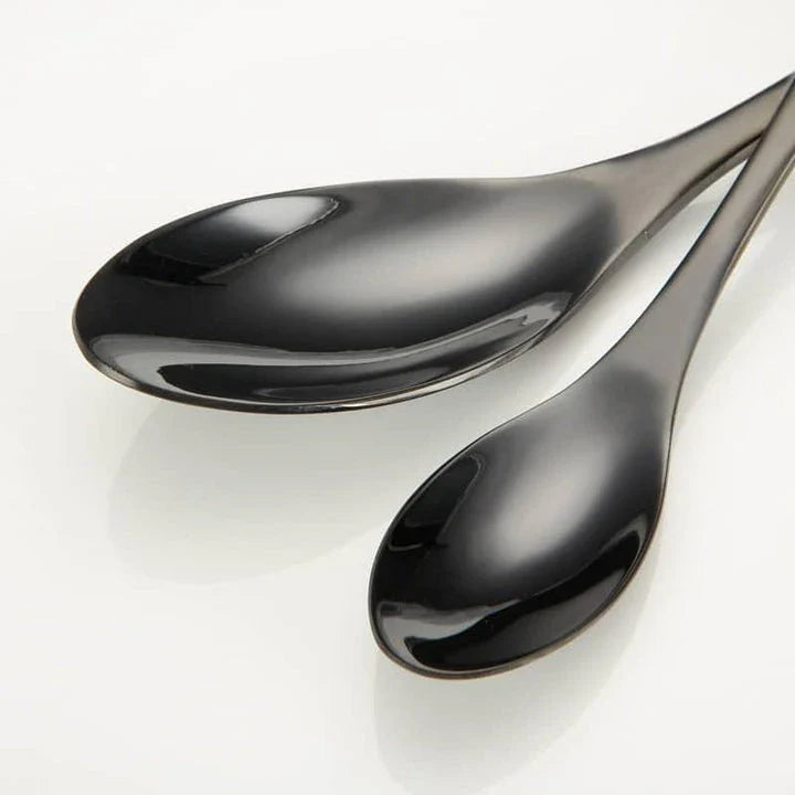 A stylish set of black stainless steel flatware, including a teaspoon, knife, and fork, on a white background.