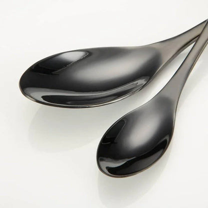 A stylish set of black stainless steel flatware, including a teaspoon, knife, and fork, on a white background.