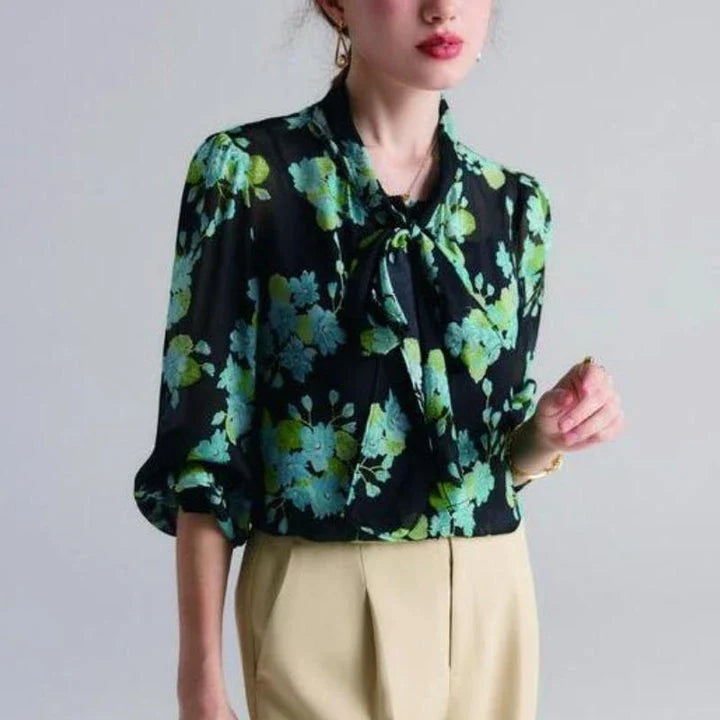 A close-up view of an elegant floral silk blend blouse with puff sleeves and a bow collar, showcasing its sophisticated British design.