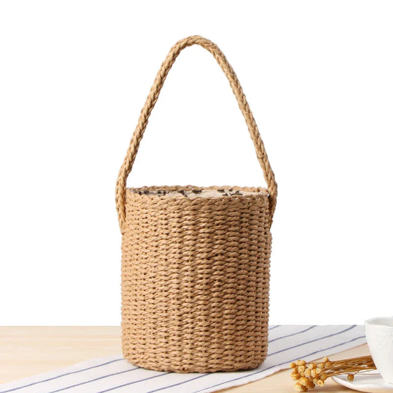 Elegant hand-crafted straw bucket bag in camel or beige, featuring a compact and lightweight design for versatile British summer style