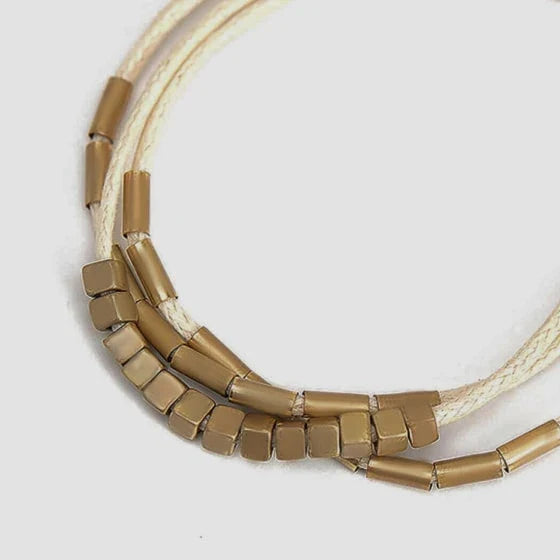 Stylish multilayered bracelet with beige leather ropes and gold-coloured beads, a modern and sophisticated accessory