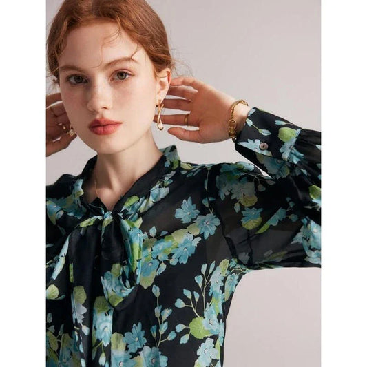 A close-up view of an elegant floral silk blend blouse with puff sleeves and a bow collar, showcasing its sophisticated British design.