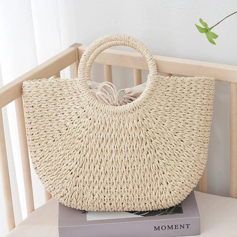 Premium handwoven straw beach tote with a casual half-moon shape and secure string closure, perfect for summer outings