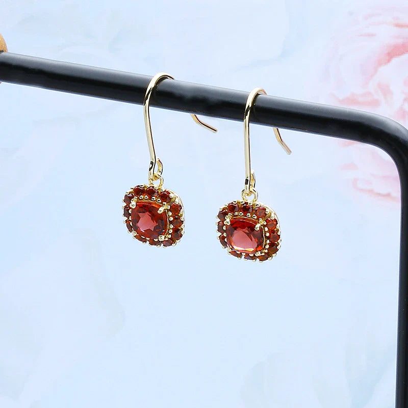 A pair of elegant red pomegranate-inspired earrings with a silver finish and geometric design, showcasing British style and sophistication.