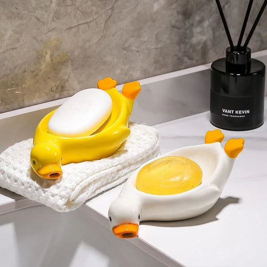 A yellow duck-shaped ceramic soap dish with a drainage system, suitable for modern and traditional British bathrooms.
