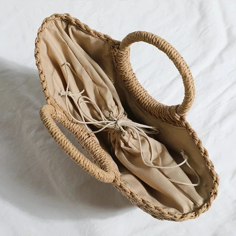 Premium handwoven straw beach tote with a casual half-moon shape and secure string closure, perfect for summer outings