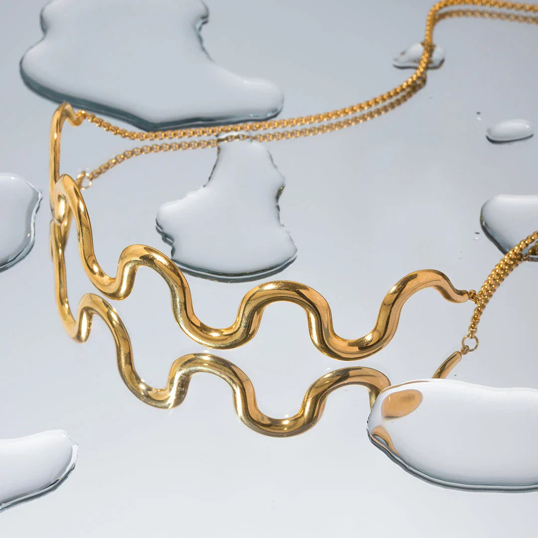 Elegant 18K gold-plated stainless steel wave bracelet and necklace set for women, showcasing a unique contemporary design with adjustable drawstring closure