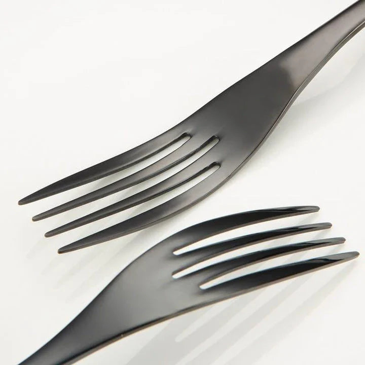 A stylish set of black stainless steel flatware, including a teaspoon, knife, and fork, on a white background.