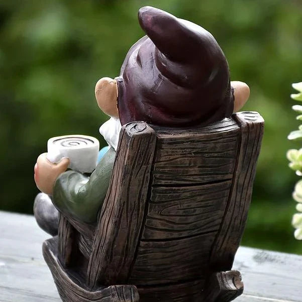 A charming garden gnome ornament made of durable resin, sitting in a rocking chair and sipping tea, adding whimsical personality to an outdoor space