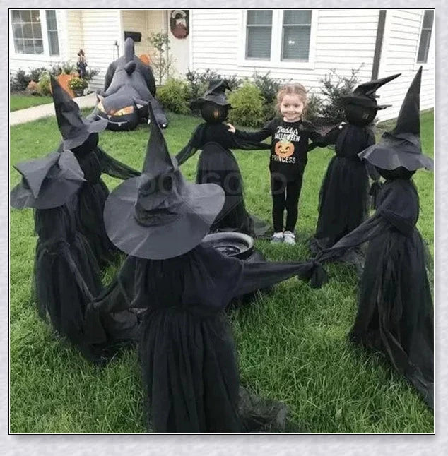 Three tall, black-robed witch figures with faceless glowing heads, standing together and holding hands, creating a spooky outdoor Halloween display