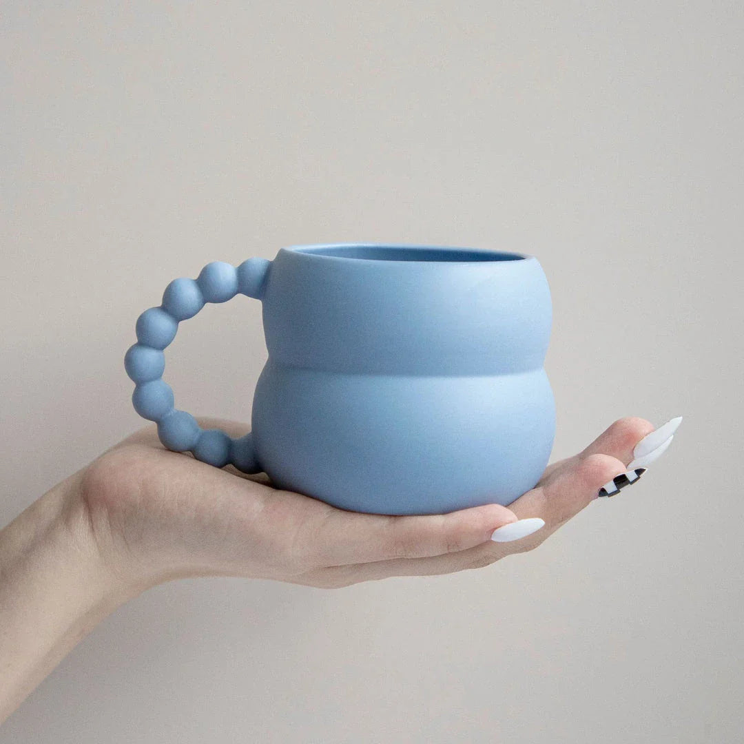 Handmade ceramic mug in beige and blue Nordic-inspired design, with a comfortable handle for enjoying hot or cold beverages.