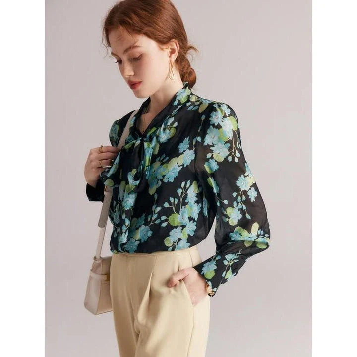 A close-up view of an elegant floral silk blend blouse with puff sleeves and a bow collar, showcasing its sophisticated British design.