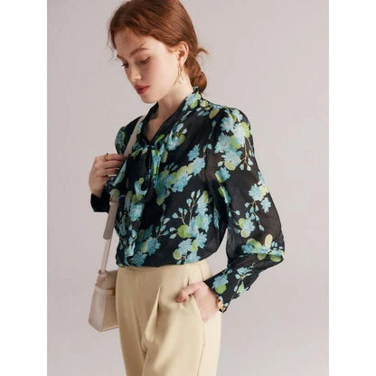 A close-up view of an elegant floral silk blend blouse with puff sleeves and a bow collar, showcasing its sophisticated British design.